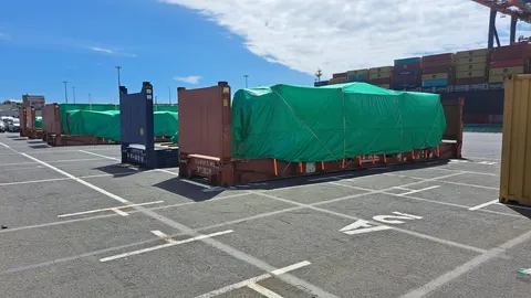 Colis hors gabarit bâchés et arrimés sur des flat racks devant un porte-conteneurs au port — IFTL