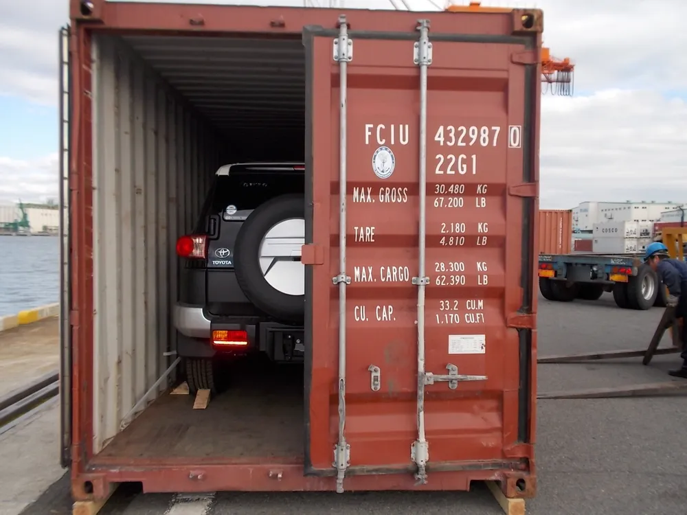 Véhicule en conteneur de groupage, voiture calée sur des cales en bois, portes du conteneur ouvertes sur le quai — chantier réel IFTL