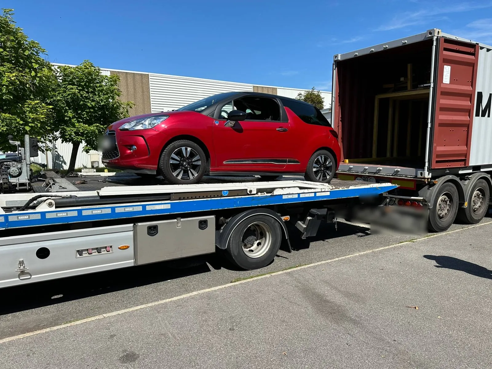 Dépôt IFTL de Paris : conteneur maritime portes ouvertes, resté sur son châssis routier, et dépanneuse-plateau qui amène une voiture à hauteur de son plancher pour la charger