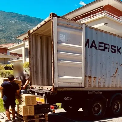 Conteneur maritime resté sur son châssis routier devant une maison, chargé depuis des palettes — chantier réel IFTL