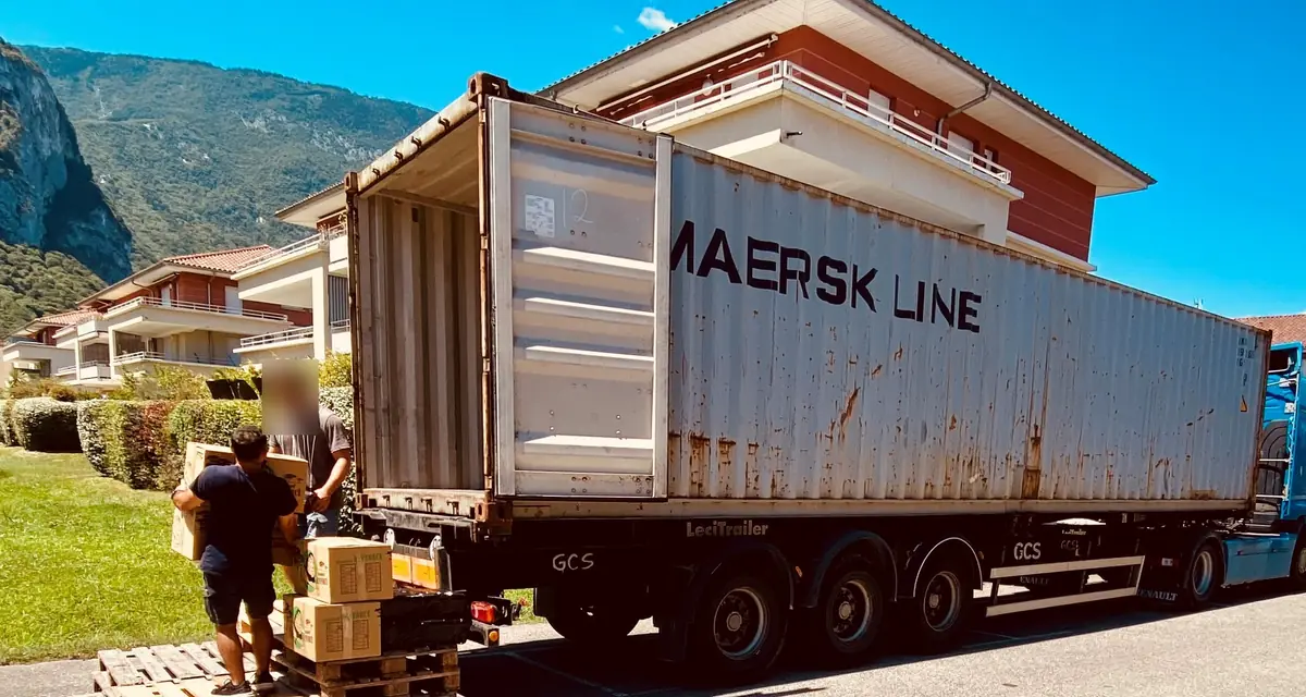 Conteneur maritime 40 pieds resté sur la remorque du camion devant une résidence, portes ouvertes, chargé à la main depuis des palettes posées au sol